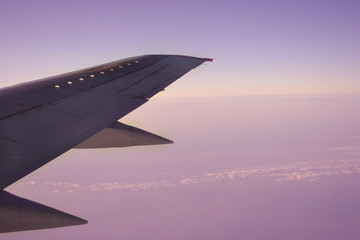 Fototapeta premium Wing of an airplane flying above the morning clouds