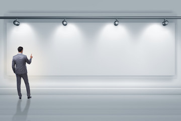 Businessman pressing virtual button on the wall lit with spotlig