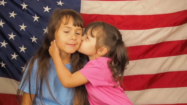 Happy sisters kiss each other against the background of the American flag.