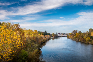 River view with trees in autumn colors on both banks. A bridge is crossing the river in the...