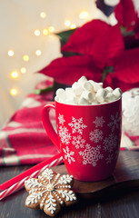 Close-up of a mug with a hot drink, marshmallow and gingerbread. Christmas decor with a bright garland and poinsettia. Selective focus, shallow depth of field, background