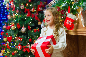 Little girl sitting by the tree holding a Christmas gift a lot o