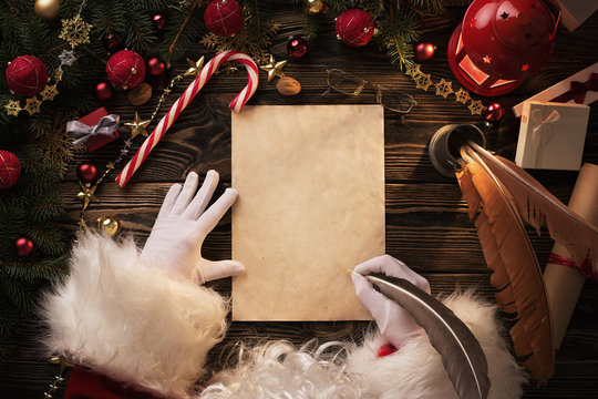 Close up of Santa Claus hands writing letter on wooden desk with copy space