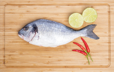 Raw Sea Bream on a Bamboo Cutting Board with Fresh Lime and Small Red Chili Peppers