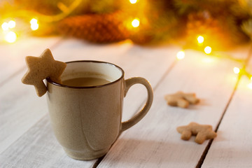 Cocoa or hot chocolate with cinnamon and gingerbread on a background with spruce branches, cones and garland.