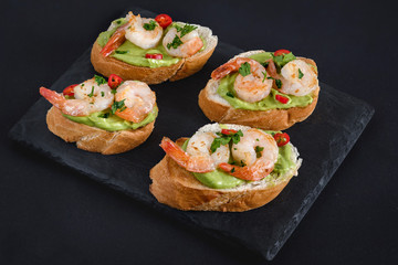 Bruschetta italian snack sandwiches with avocado cream and prawns decorated by parsley and chilli peppers.