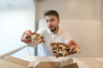 The man holds two pieces of pizza in his hands and sends them to the camera. A man offers a pizza. A delicious pizza in the hands of a guy.