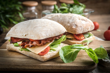 Ciabatta sandwich with arugula salad, bacon and yellow cheese.