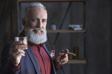 Cheer. Portrait of smiling elegant bearded old businessman tasting appetizing alcohol and keeping tobacco. Celebration concept