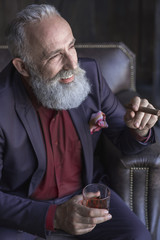 Portrait of happy unshaven old businessman drinking brandy while smoking cigar. Relax concept