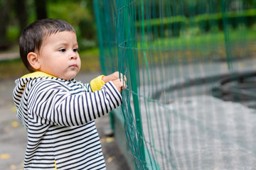 Little sad latin boy trying to break a metal fence.
