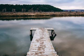 Fototapeta premium Wooden pier or jetty on blue lake sunset and sky reflection water