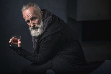 Portrait of beaming bearded old man tasting alcohol while keeping beads in hand. Relax concept