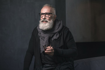 Portrait of laughing unshaven senior drinking appetizing liquid while locating in apartment. Leisure concept. Copy space