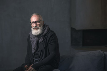 Portrait of smiling bearded old man tasting delicious beverage while situating in room. Cheerfulness concept. Copy space