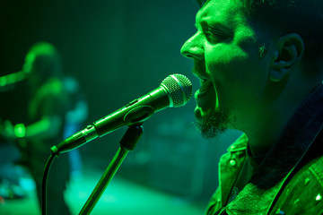 Bearded singer sings at a microphone on concert, with green light