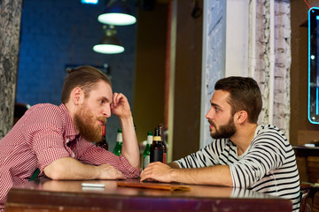 Side view portrait of two modern young men chatting casually sitting at table in bar and drinking...