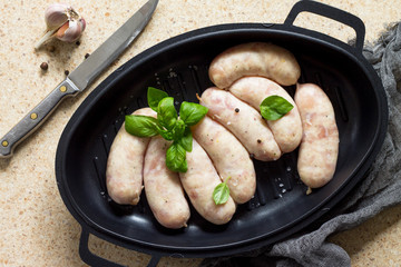 Raw homemade sausages on slate background, with basil and spices.