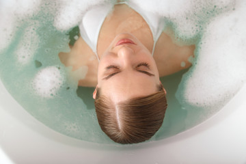 Top view of relaxed young woman enjoying warm water with bubbles. She is lying in bathtub with pleasure