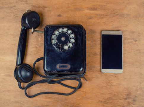 Black vintage phone and a new modern mobile phone on an old wooden background, top view, retro style (old and new concept)