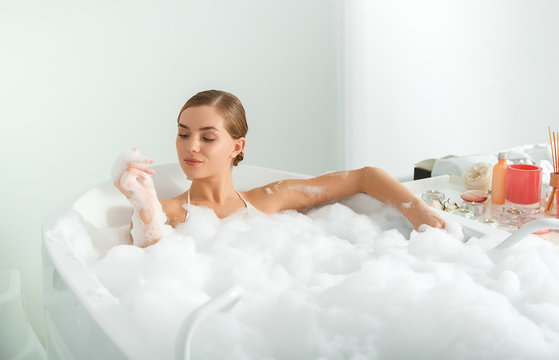 Confident girl is taking a bath with bubbles. She is looking at her clear hand with satisfaction. Luxury concept