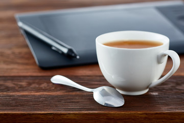 Digital tablet and cup of coffee on wooden desk. Simple workspace or coffee break in morning selective focus