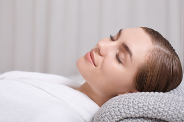Fototapeta premium Side view of relaxed young woman lying on massage table with enjoyment. Her eyes are closed with gentle smile