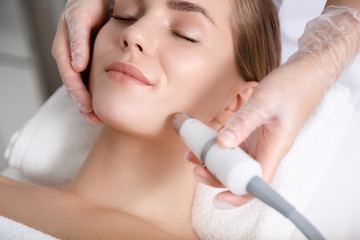 Close up of beautician hand making ultrasound facial procedure by special equipment. Her closed...