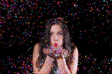 A young girl stands in front of a black background and is surrounded by confetti explosions. She laughs and smiles in her role as a celebration girl.