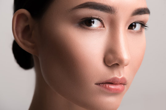 Close-up of face of young asian woman with perfect and soft skin. She is looking at camera dreamily. Isolated background