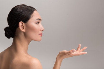 Perfect skincare and beauty concept. Side view profile of positive attractive young asian woman is holding palm up and looking ahead with slight smile. Isolated with copy space in the right side
