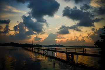 Fototapeta na wymiar old wooden bridge on tropical lake to island at sunrise