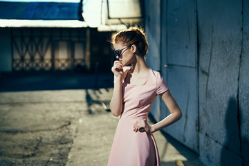 Young beautiful woman in sunglasses and in a pink dress outdoors in the city