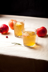 Two vintage glasses with apple cider on black background. Christmas beverages concept. Two red apples and rosemary sprig aside.  Warm backlight. Vertical composition.