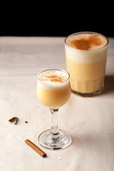 Two glasses with christmas eggnog drink decorated with cinnamon on dark background. Vertical composition.