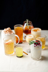 Set of various winter cocktails: mulled wine, eggnog, limoncello, old-fashioned, coconut margarita. Black background, white linen tablecloth.