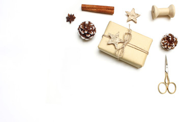 Christmas festive styled stock image composition. Handmade gift box with wooden and anise stars, cinnamon, spice sticks, pinecones and golden scissorson white wooden background. Top view.