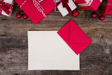 Christmas gift giving and list to Santa Claus concept - christmas presents in red paper boxes on wooden table, flat lay with copy space on empty paper note
