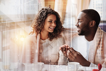 Unpredictable present. Young positive man putting a wedding ring on his womans finger while looking...