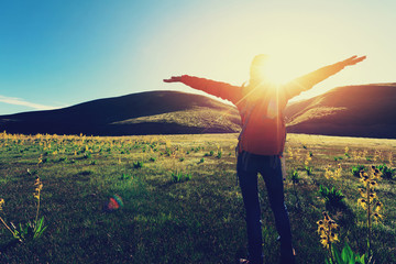 happy woman hiker raised arms  in sunrise mountains