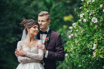 Beautiful couple of happy stylish newlyweds on a walk in the sunny summer park or garden on their wedding day