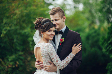 Fototapeta premium Beautiful couple of happy stylish newlyweds on a walk in the sunny summer park or garden on their wedding day