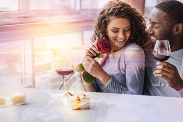Emotions. Young pleasant girl looking down while her boyfriend holding a glass of wine and looking at her with love
