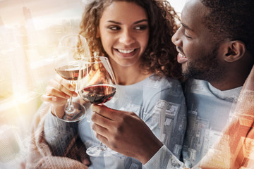 Happiness in eyes. Close up of young pleasant couple sitting close to each other while holding glasses with wine and expressing delight