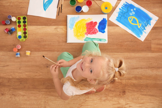 Cute girl painting picture on sheet of paper, indoors