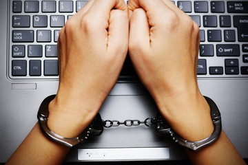 Cybercrime concept – top view of hands with handcuffs above the laptop keyboard