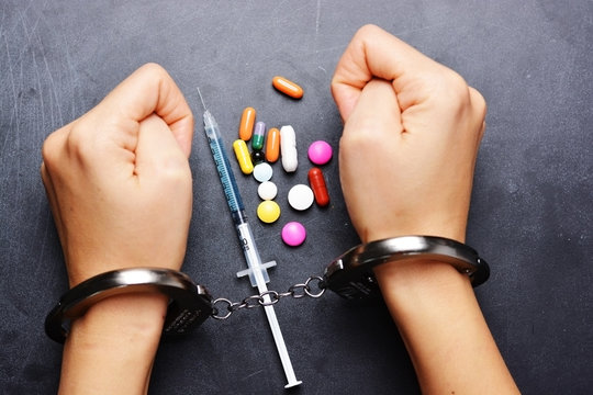 Drug dealer arrested for prohibited substances trafficking, handcuffed person with syringe and colorful pills