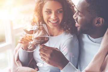 Be happy. Young loving couple sitting close to each other smiling and clinking glasses with wine