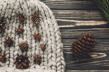 stylish christmas flat lay. woolen hat and green tree fir branches with cones and anise on rustic wooden background top view, space for text.  atmospheric hygge winter image