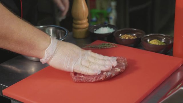 Chef marinating raw meat for preparing steak at commercial kitchen, close-up
